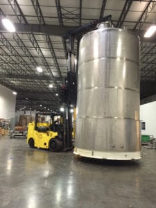 A large metal tank in a warehouse with a forklift.