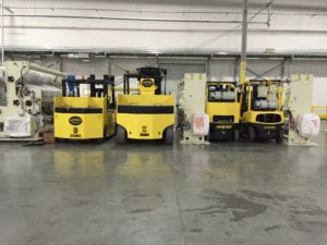 Three yellow forklifts in a warehouse with signs.