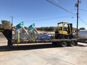 A yellow truck is pulling a trailer full of construction equipment.