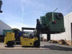 A large yellow forklift is lifting a green machine.