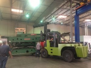 A large green truck in a warehouse with people standing around.