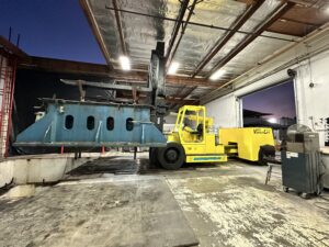 Yellow forklift moving large blue equipment indoors.