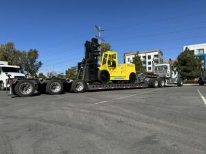 Yellow forklift on truck trailer in parking lot.