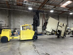 Yellow forklift lifting heavy industrial equipment indoors.