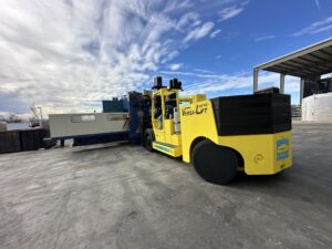 Yellow forklift moving large industrial equipment.