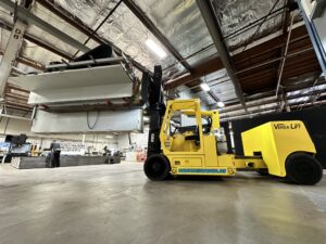 Yellow forklift lifting large equipment in warehouse.