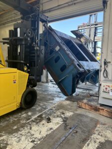 Forklift moving large metal structure indoors.