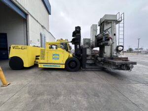 Yellow forklift moving large industrial equipment outside.