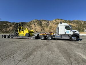 Truck transporting forklift on flatbed trailer.