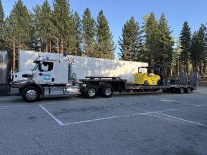 Truck transporting forklift on a flatbed trailer.
