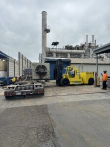 Forklift moving large equipment at industrial site.