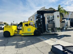 Yellow forklift transporting heavy machinery outdoors.