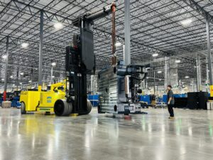 Forklift moving machinery inside large warehouse.