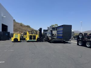 Forklift moving large equipment outdoors.