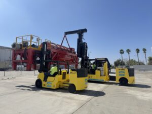 Yellow forklifts lifting large red machinery piece.