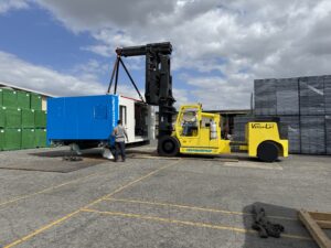 Yellow forklift lifting blue container outdoors.