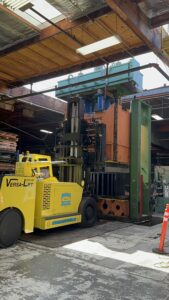 Forklift moving large industrial machinery indoors.