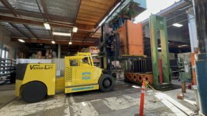 Yellow forklift lifting heavy machinery in warehouse.